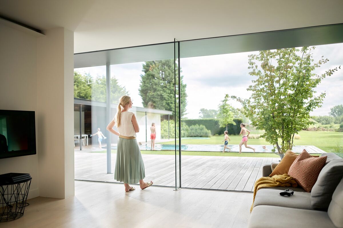 Woman indoors, standing in front of large sliding window.