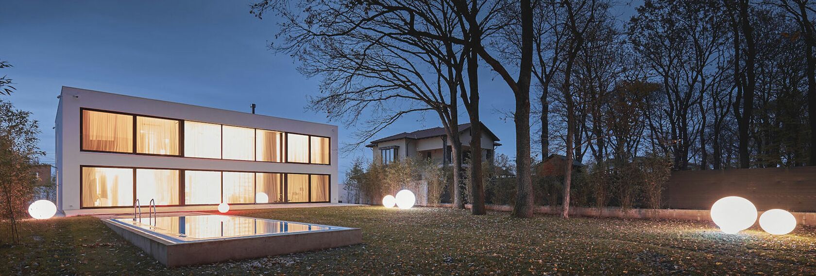 Vue extérieure d'une maison privée roumaine blanche dont les fenêtres sont éclairées par des lumières vives.
