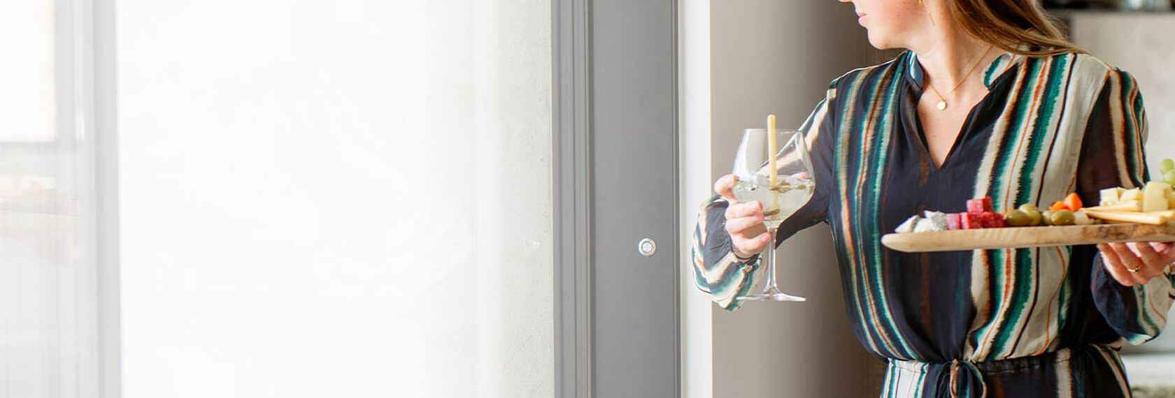 Woman holding drinks, opening a motorised sliding door with a push button on the wall.