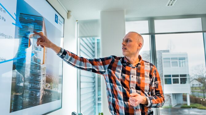 White man in plaid shirt pointing at presentation screen.