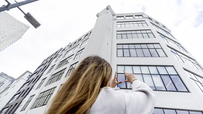 Femme tenant une batterie de secours - lève les mains vers un bâtiment blanc de taille moyenne avec beaucoup de FENETRES.