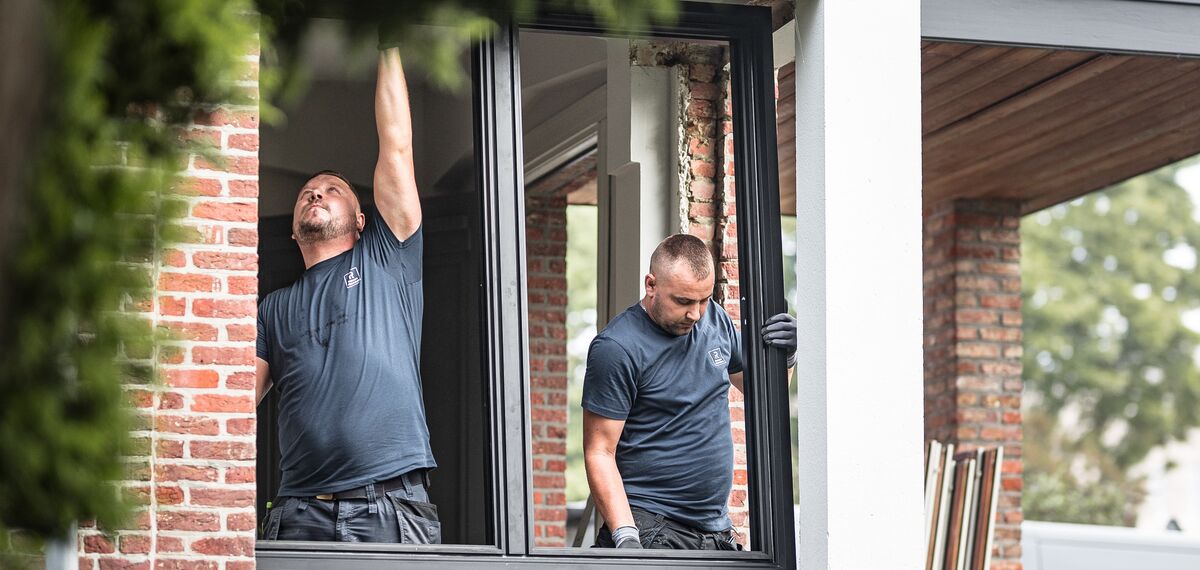Deux installateurs posant de nouveaux profils en aluminium dans une maison rénovée.