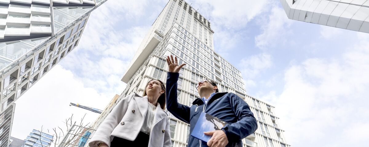 Homme et femme devant un gratte-ciel pointant le ciel