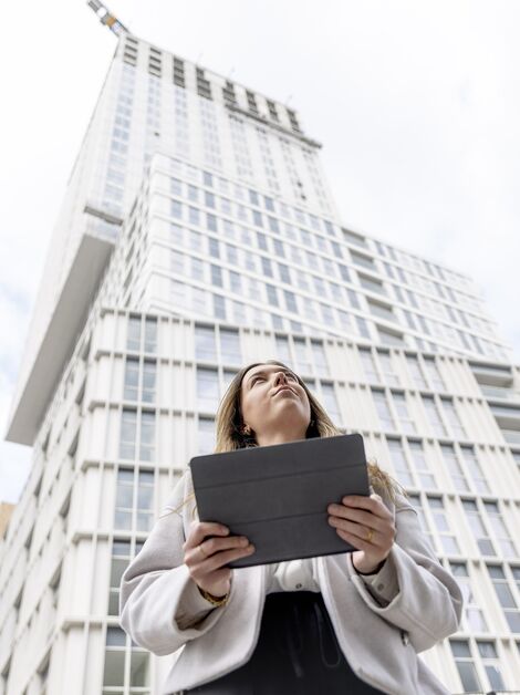 Femme blonde tenant un iPad à la recherche d’une batterie de secours - monte vers un immeuble d’appartements blanc.