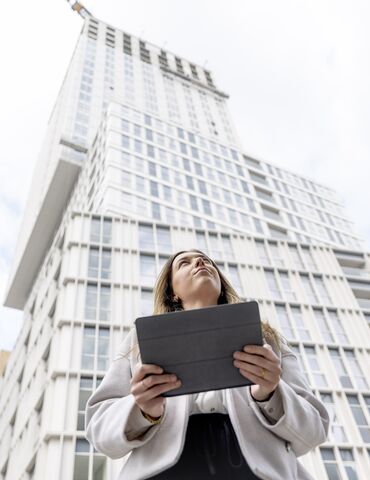 Femme blonde tenant un iPad à la recherche d’une batterie de secours - monte vers un immeuble d’appartements blanc.
