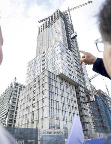 Man and woman pointing at grey high-rise project under construction.
